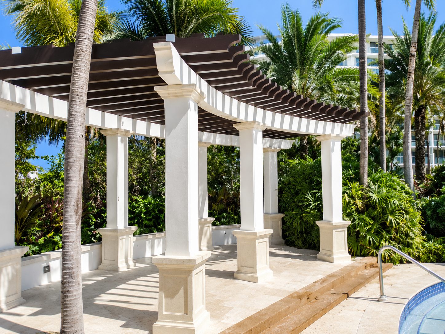 White columned pergola with dark slatted rafters curving around a resort pool deck