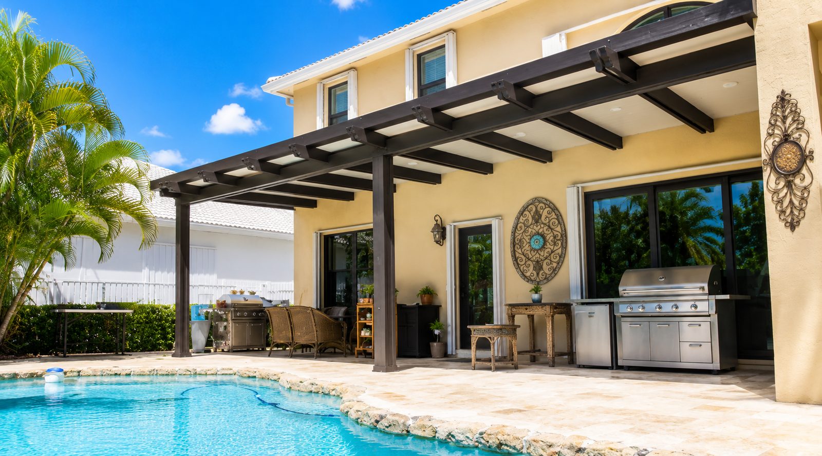 Bronze aluminum patio cover with open rafters attached to a home along a pool deck