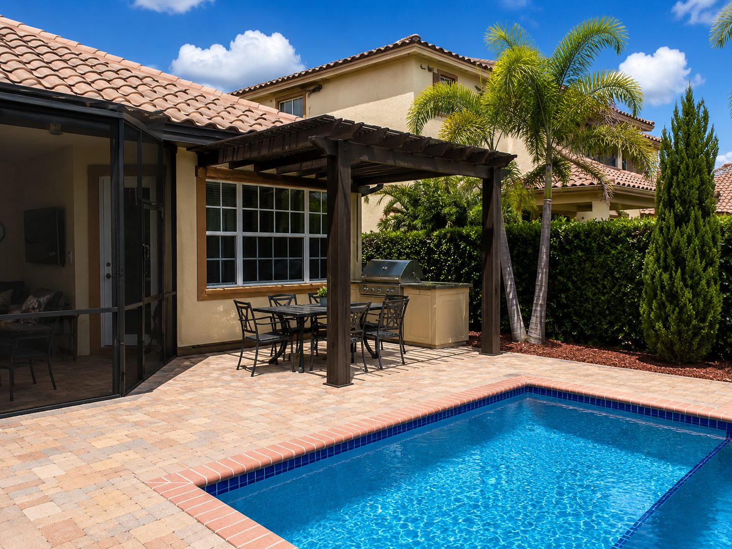 Dark aluminum pergola over a dining table and grill station beside a pool